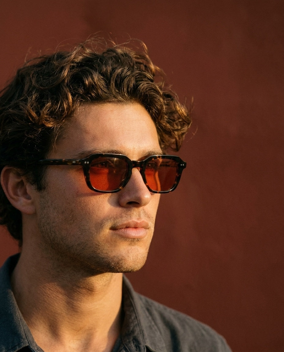 curly hair man amber sunglasses red wall_4x5