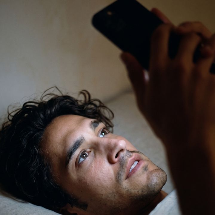 Late night in bed, face lit by his phone